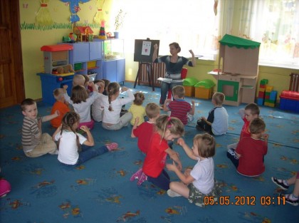 dzieci siedzące na dywanie słuchające swojej wychowawczyni