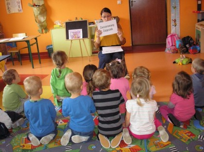 dzieci klęczące na dywanie słuchają swojej opiekunki