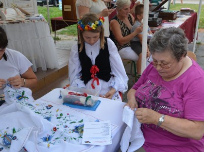 starsza Pani z dzieckiem wyszywa obrusy